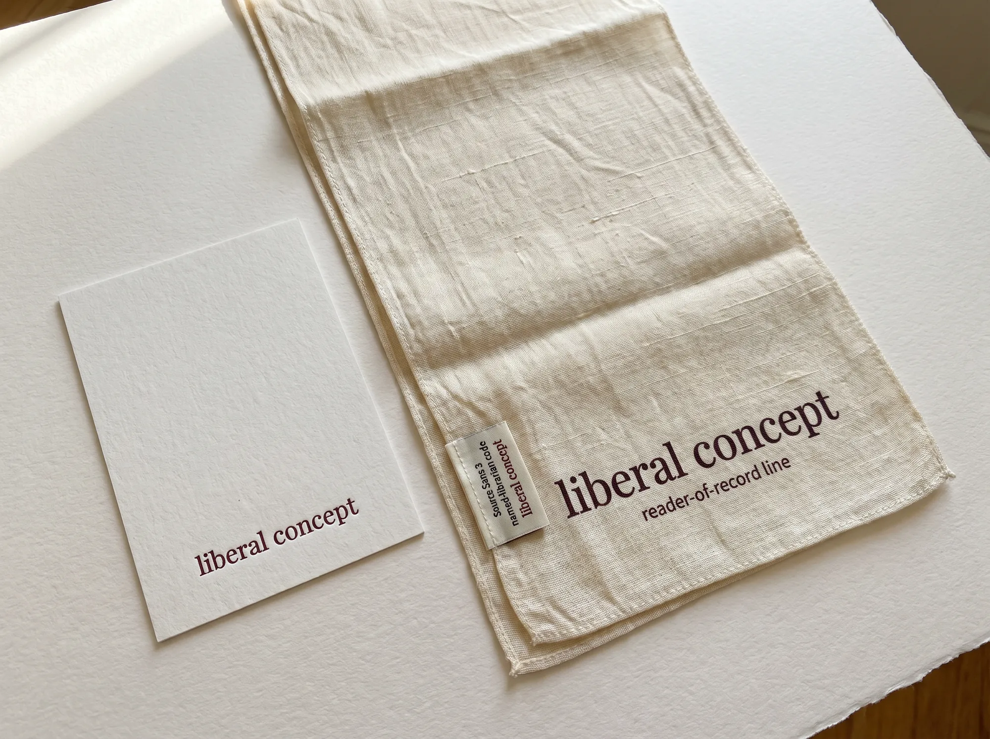 Liberal Concept Reader Silk Scarf (Fine Stationery & Reading Tools) — A long hand-loomed silk reader scarf in warm cream with the wordmark hand-printed in deep wine at one end — a working accessory issued to working journalists and named librarians at the working close.